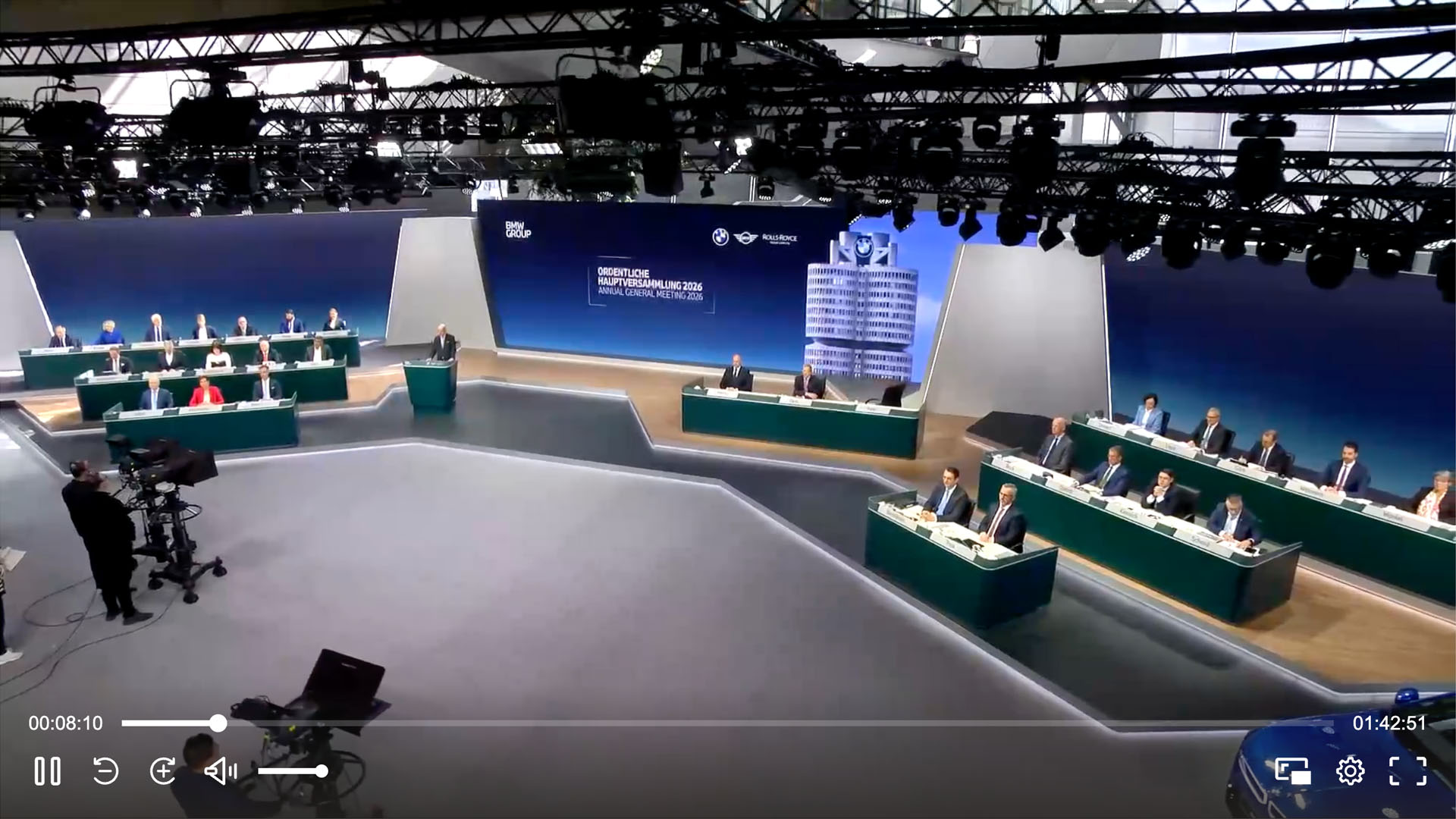 Livestream-Videoplayer zeigt eine Hauptversammlung auf einer Bühne mit BMW-Group-Branding und sitzenden Vorstandsmitgliedern und Aktionären